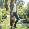 front view of Brown Backpack, backpack on model outdoors, flowers in the background, Addie Leather Backpack.